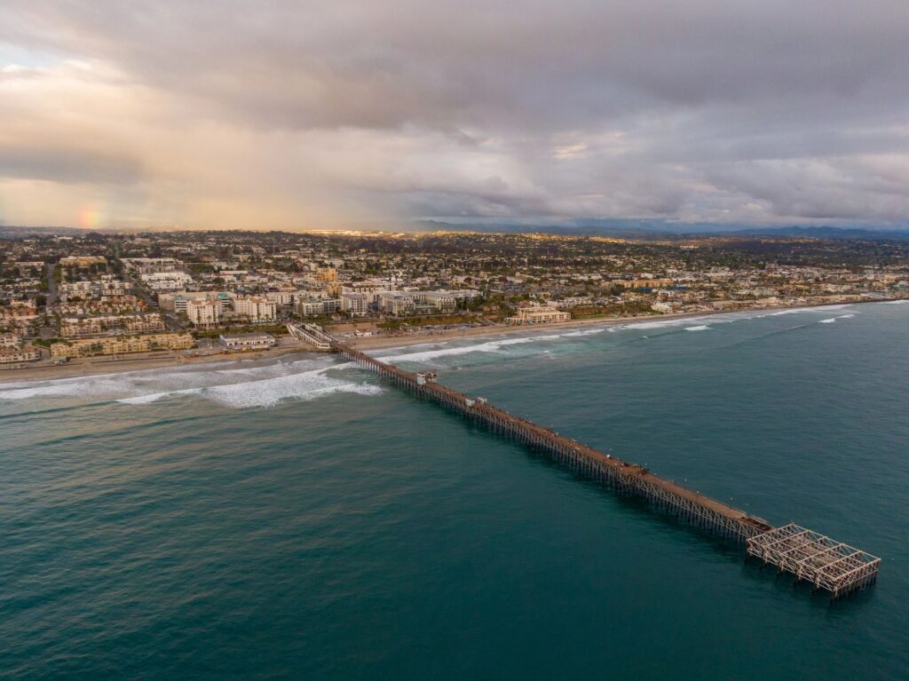 High Angle Aerial Drone View of Oceanside Pier and California Coastline with Distant Rainbow